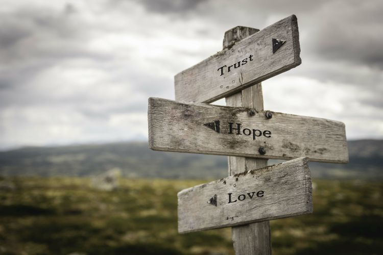 A signpost with three signs saying "Trust", "Hope" and "Love"