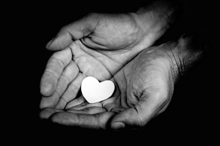 A black and white photo showing upturned hands held together with a paper heart resting on the palms