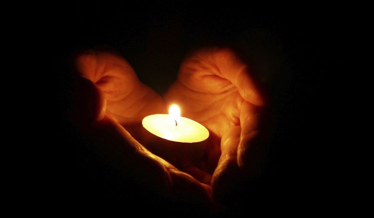 Hands shaped like a heart holding a lit candle